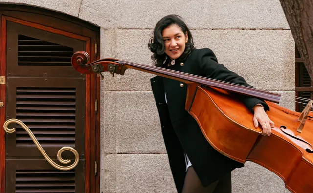 Emilse Ríos sonriendo en una calle de Madrid, con su contrabajo al hombro delante de un portal de madera